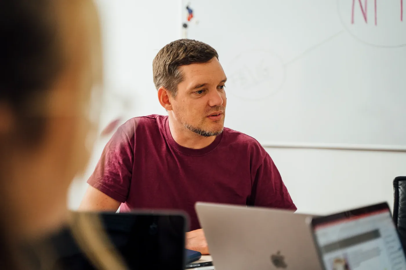 Zwei Personen stimmen sich am Schreibtisch über einen Kommentar ab, daneben laufen die Kanäle auf zwei Laptops